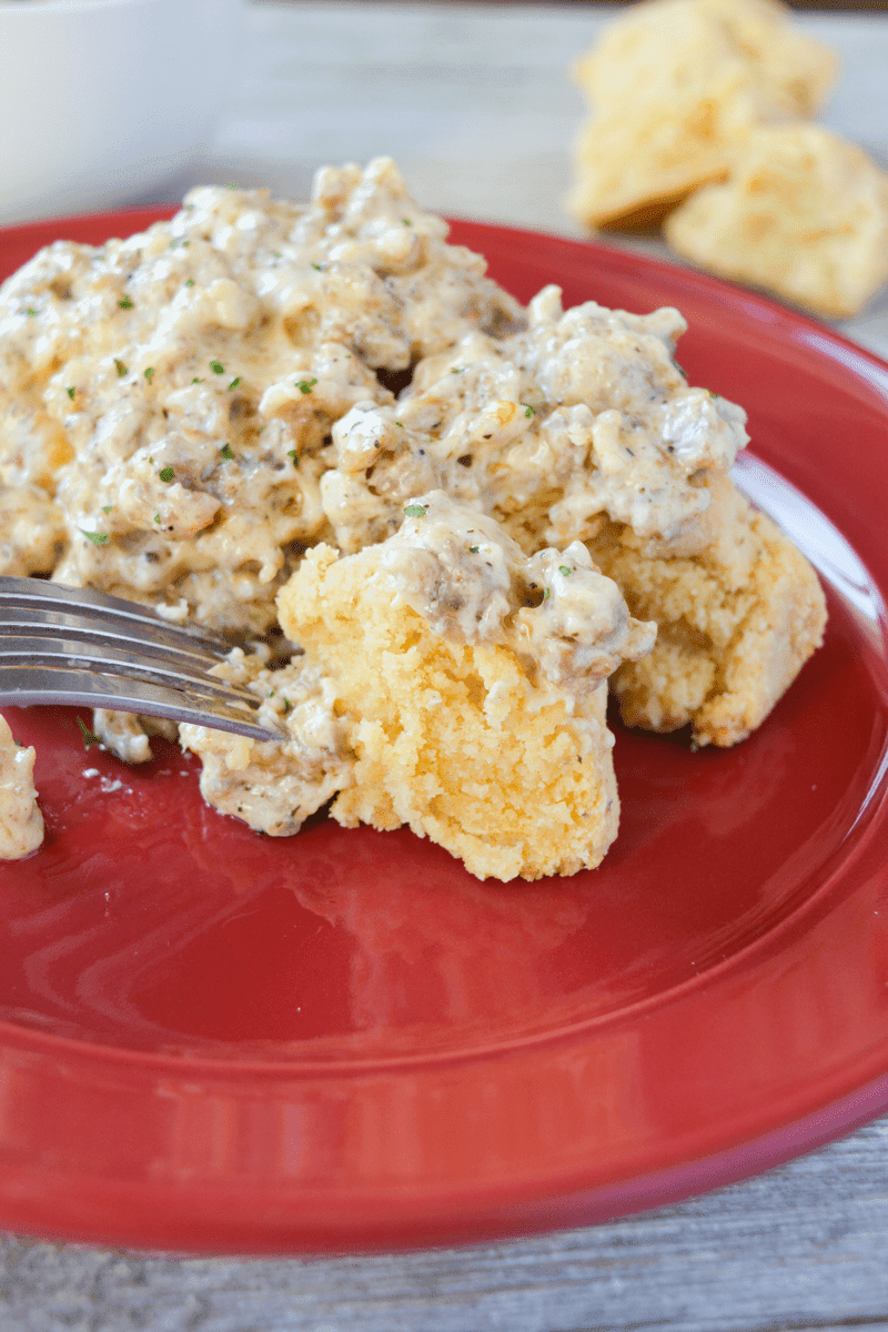 biscuits and gravy sitting on a red plate with a fork poking into the side of the meal