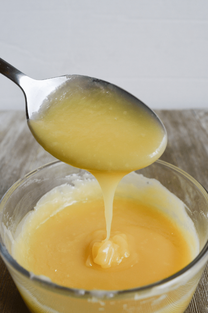 close up on keto condensed milk, dripping from a spoon into a small cup