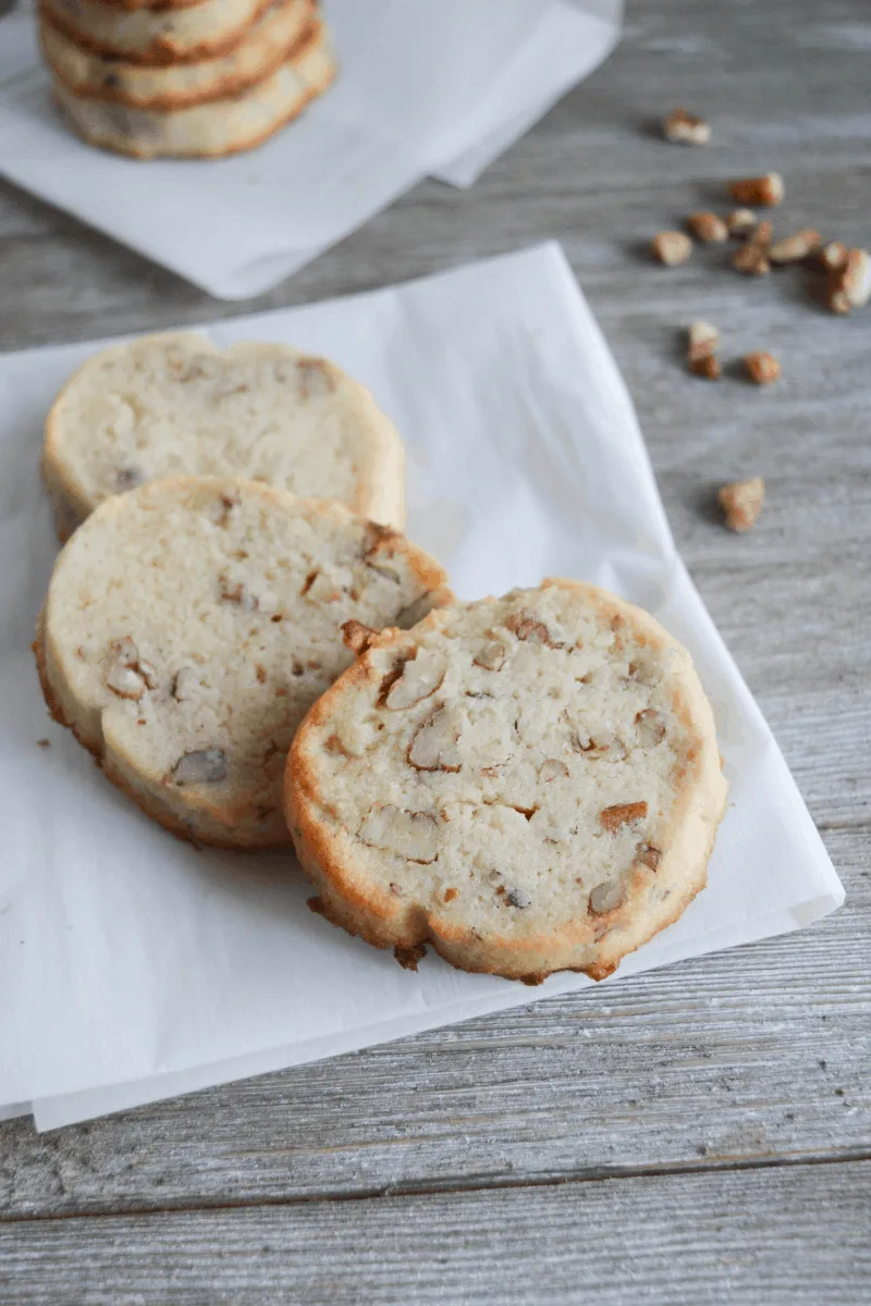 three cookies on a white napkin with pecans scattered in the background