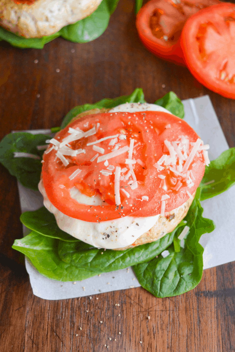 fully dressed keto chicken pesto burger with sliced tomatoes in the background