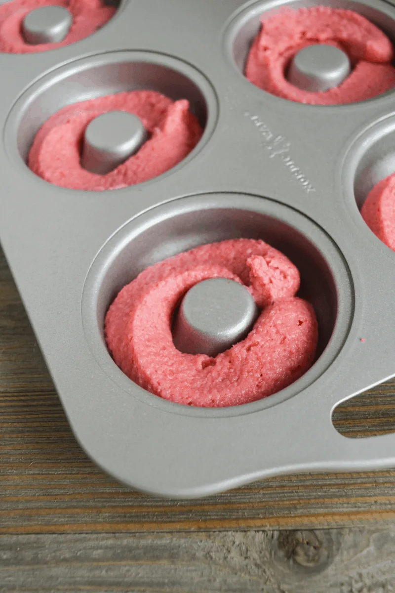 donut dough piped into metal donut pan