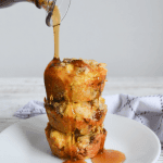 three stacked keto breakfast bombs on a white plate with syrup being poured over them