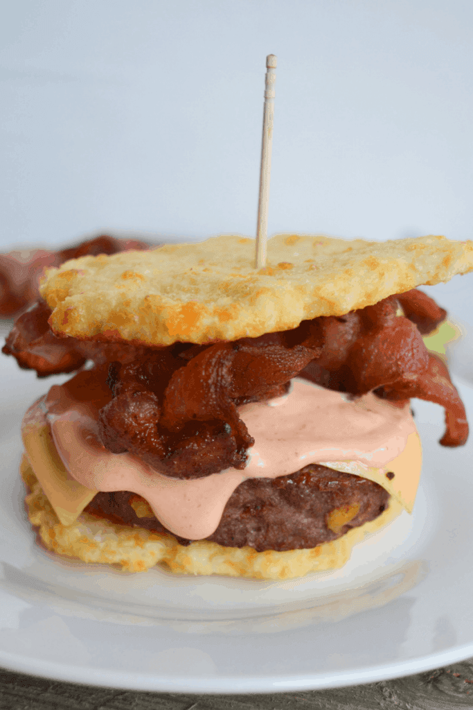 bacon cheeseburger sandwiched between two cauliflower buns on a white plate