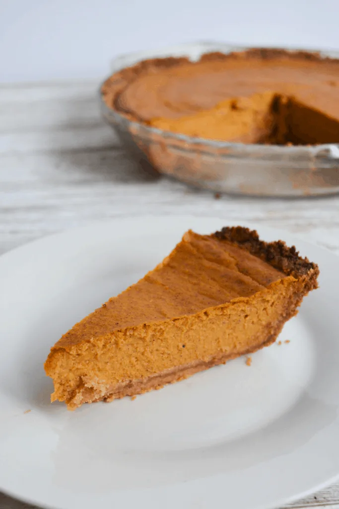 slice of pumpkin pie on white plate with full pie in the background