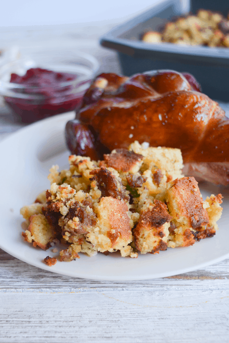cornbread stuffing on white plate with turkey leg, cranberry sauce in background