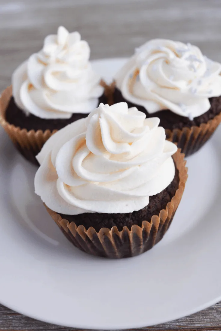 three chocolate cupcakes frosted with vanilla frosting sitting on a white plate