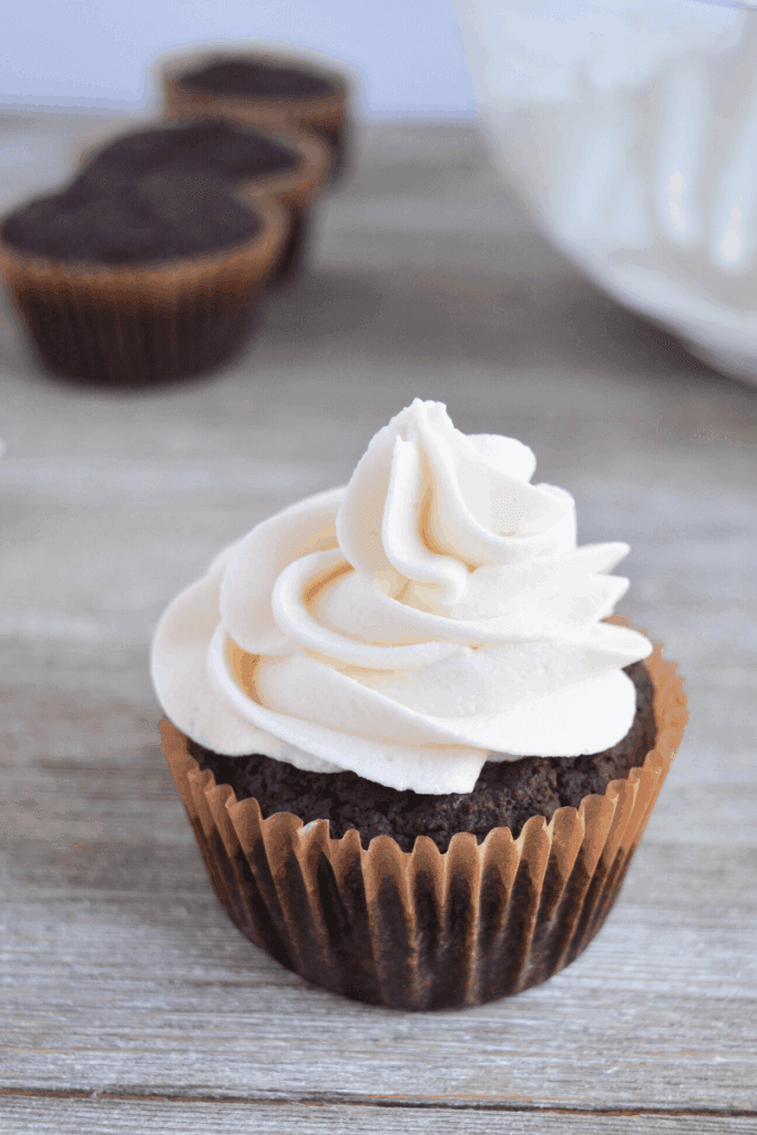 one frosted cupcake is in the foreground and 3 unfrosted cupcakes are blurred in the background