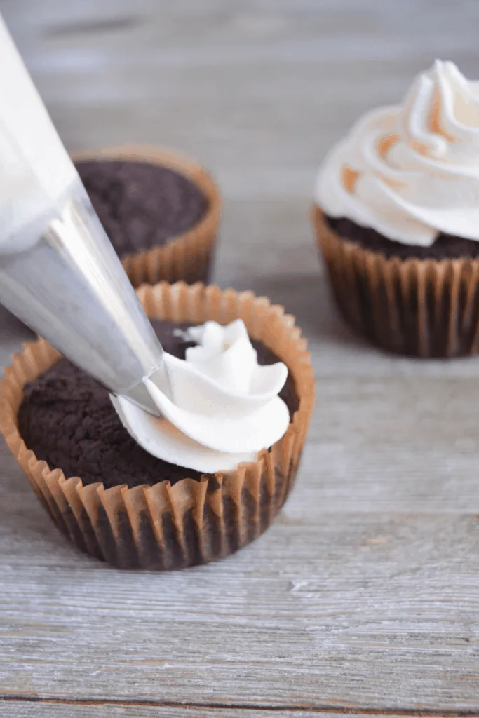 chocolate cupcake being frosted with vanilla buttercream frosting