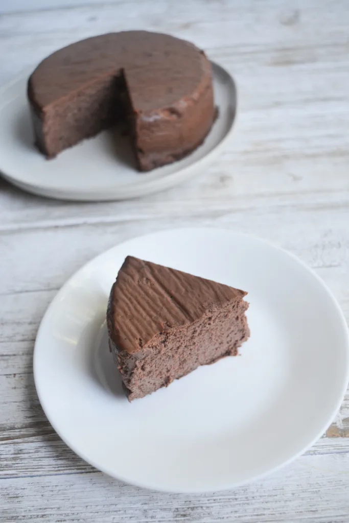 one slice of instant pot keto cheesecake in the foreground on a white plate and the rest of the cheesecake in the background on a different white plate