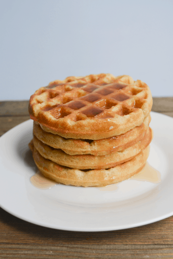 stack of keto waffles on a white plate drizzled in syrup