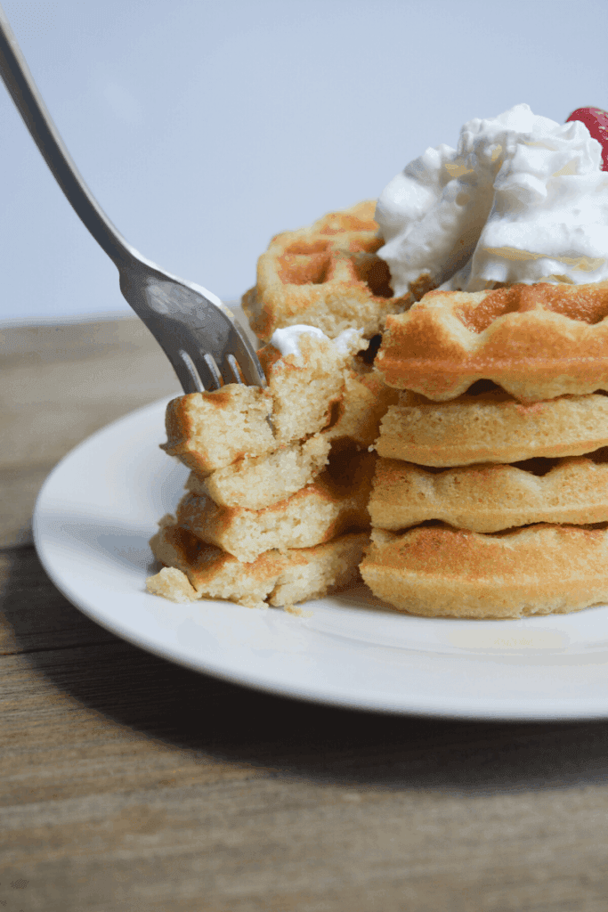 stack of keto waffles on a white plate with whipped cream and a strawberry on top