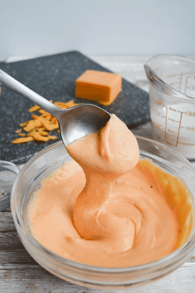 creamy keto cheese sauce dripping from a spoon into a small bowl