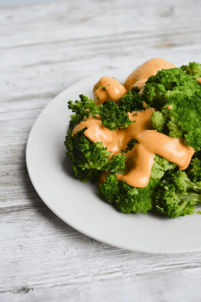 cheese sauce covering steamed broccoli on a white plate