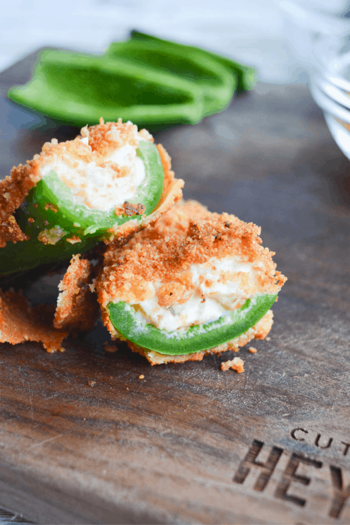 two jalapeno popper halves covered in low carb breading sitting on a cutting board 