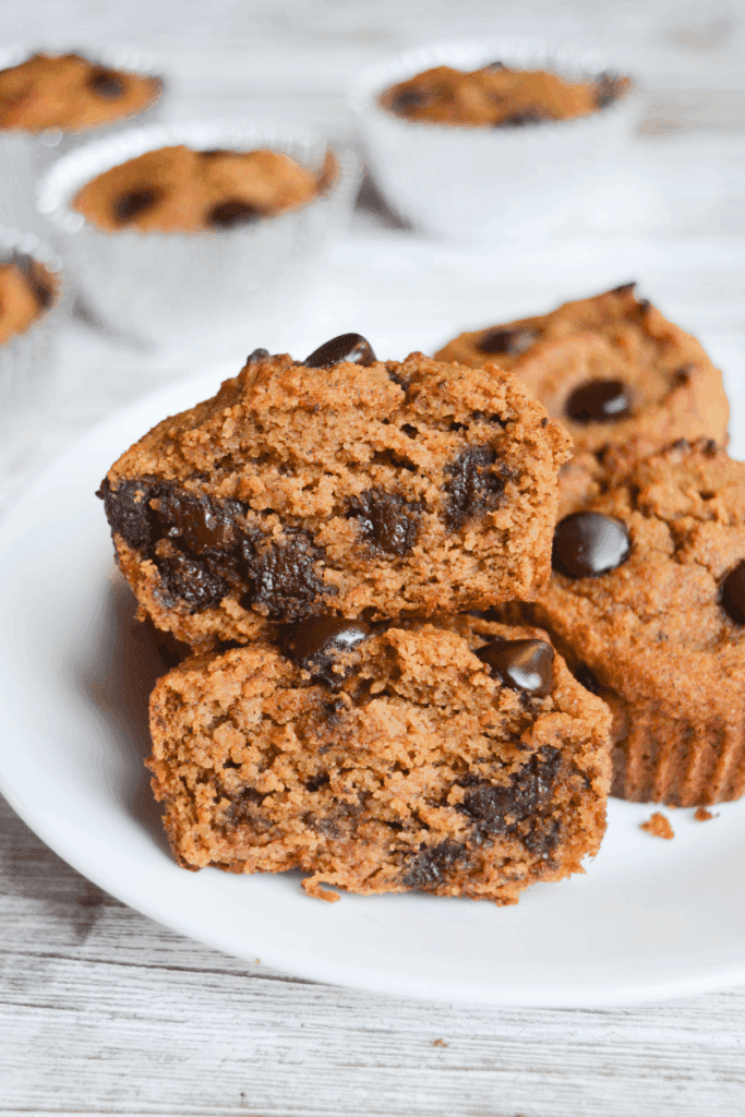 keto chocolate chip pumpkin muffins sitting on a white plate. one is cut in half and stacked to show gooey, chocolatey inside