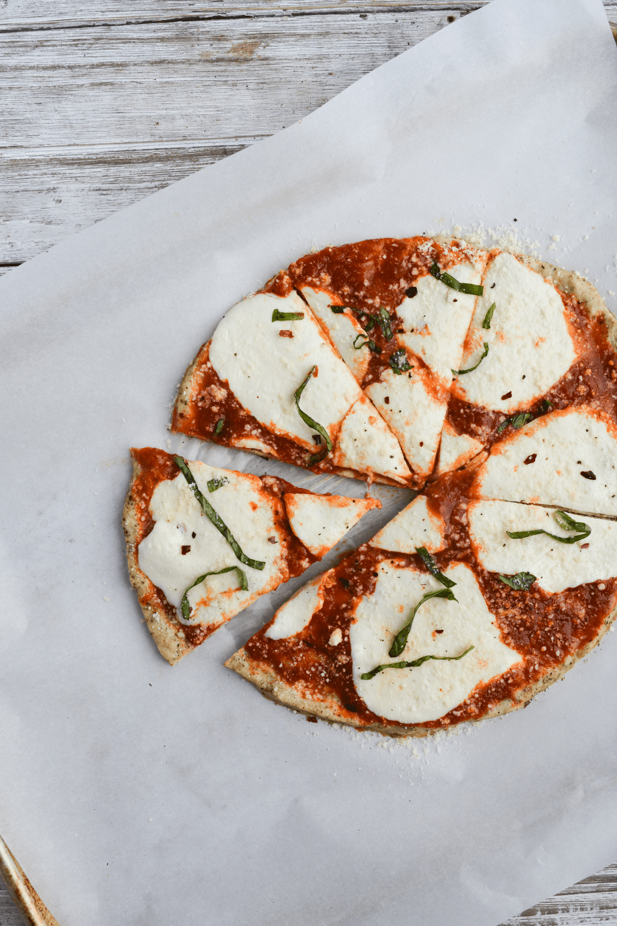 chicken parmesan pizza topped with basil, pepper, and crushed red pepper sitting on a white piece of parchment paper