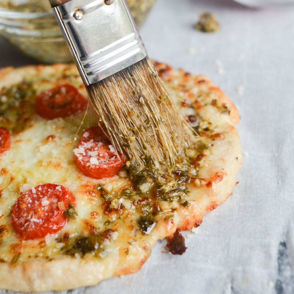 Chicken crust pizza being brushed with basil pesto