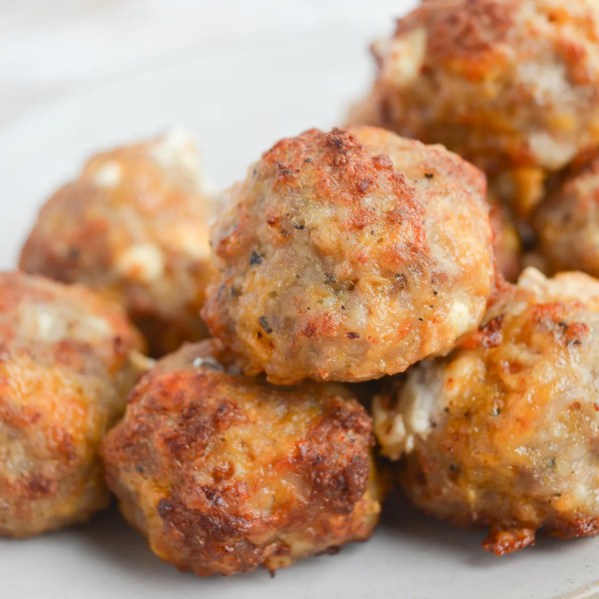 several cheese and sausage balls stacked on a plate. cream cheese is oozing out of some of them