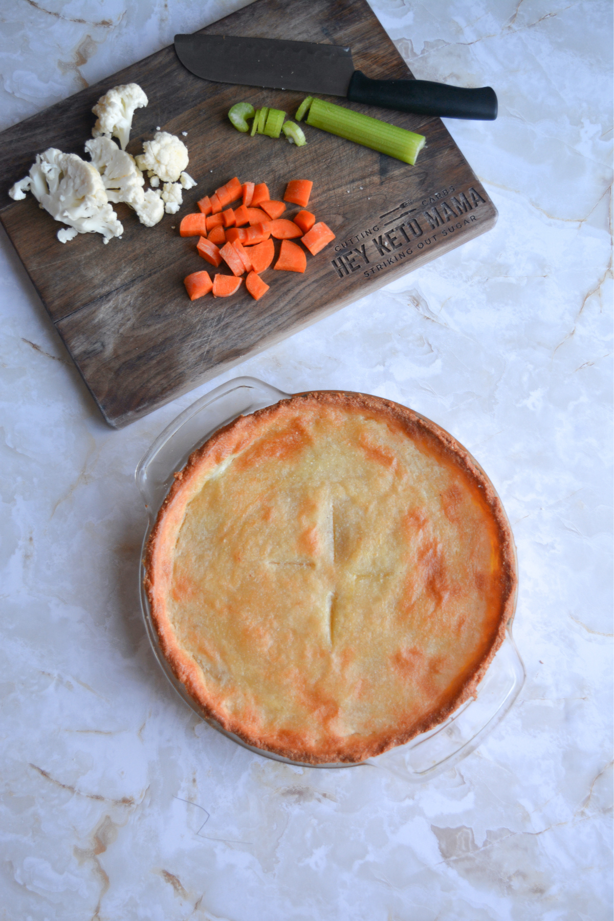cooked keto chicken pot pie sitting separately from chopped ingredients (cauliflower, carrots and celery) on a cutting board