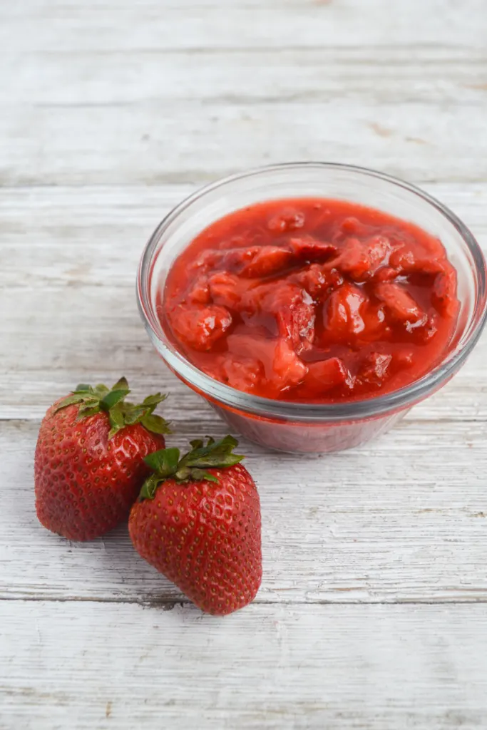 small bowl of homemade strawberry jam with 2 strawberries to its side