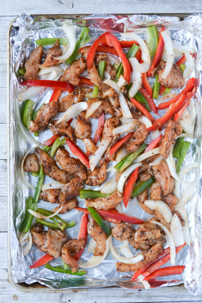 cooked sheet pan chicken fajitas sitting on the aluminum foil-covered pan