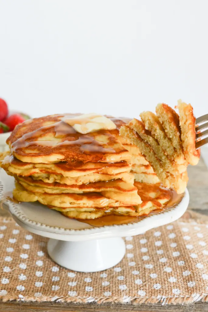 close up on a stack of coconut flour keto pancakes, covered with sugar free syrup and a pat of butter, with a slice of the stack being taken away with a fork
