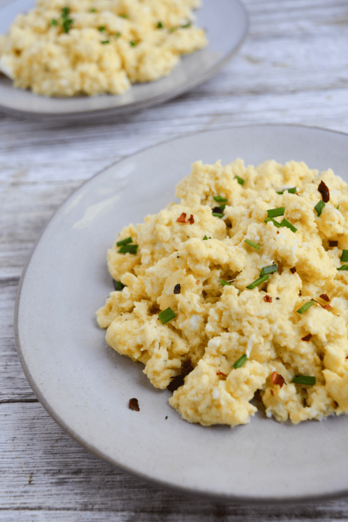 plate of fluffy scrambled eggs garnished with chopped chives and crused red pepper