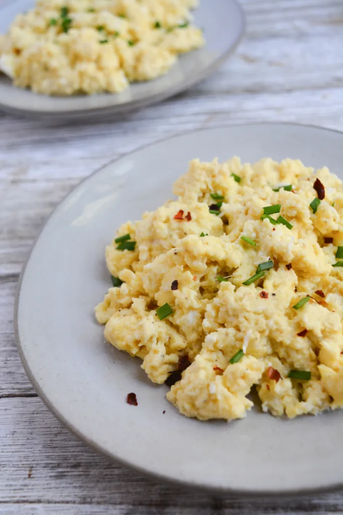 plate of fluffy scrambled eggs garnished with chopped chives and crused red pepper