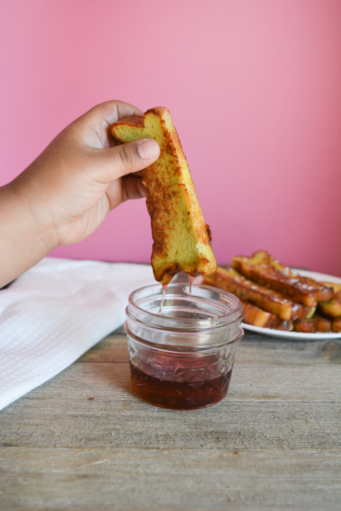 hand dipping keto french toast stick into small cup of syrup