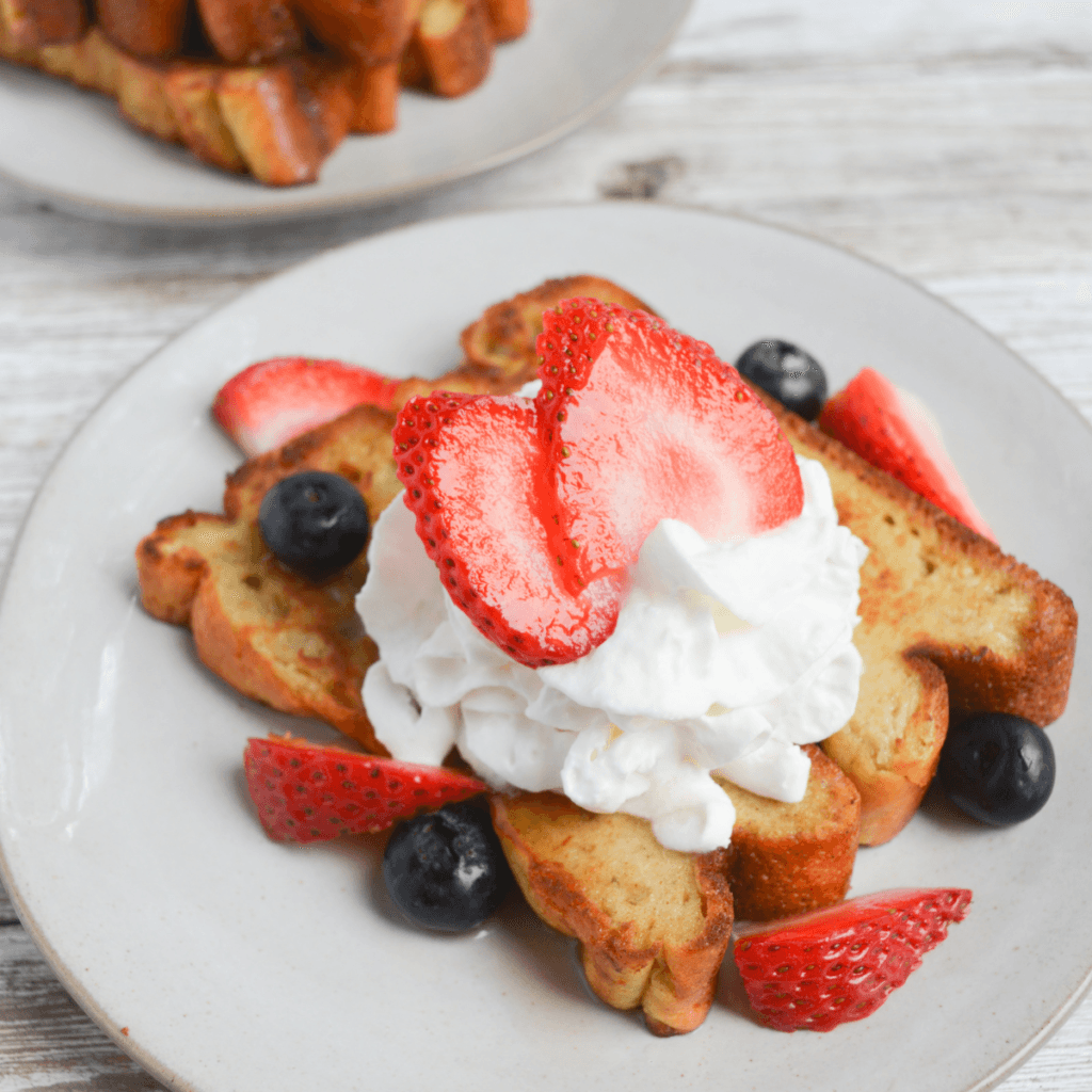 close up of keto french toast sticks topped with sliced strawberries and blueberries