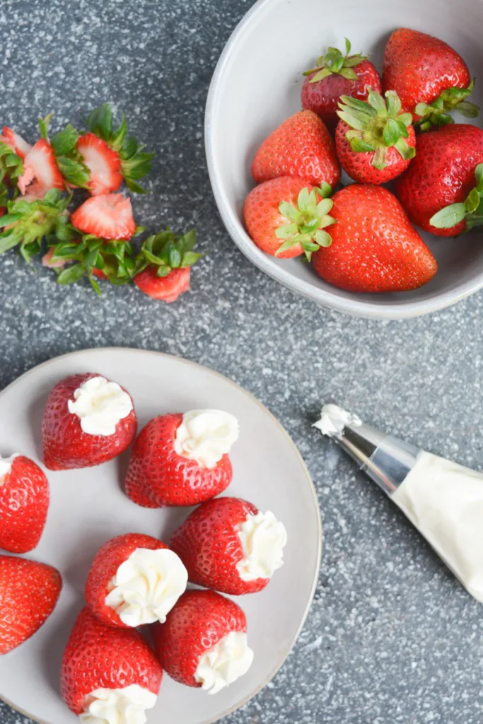 plate of cheesecake stuffed strawberries on a cutting board with a piping bag