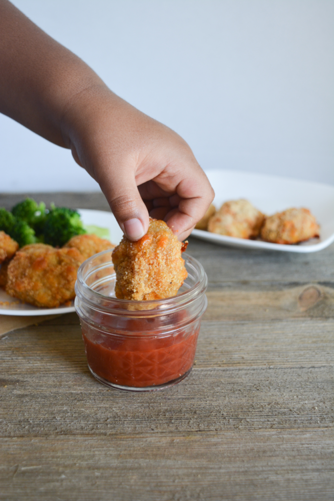child's hand dipping a keto chicken nugget into a small bowl of sugar free ketchup