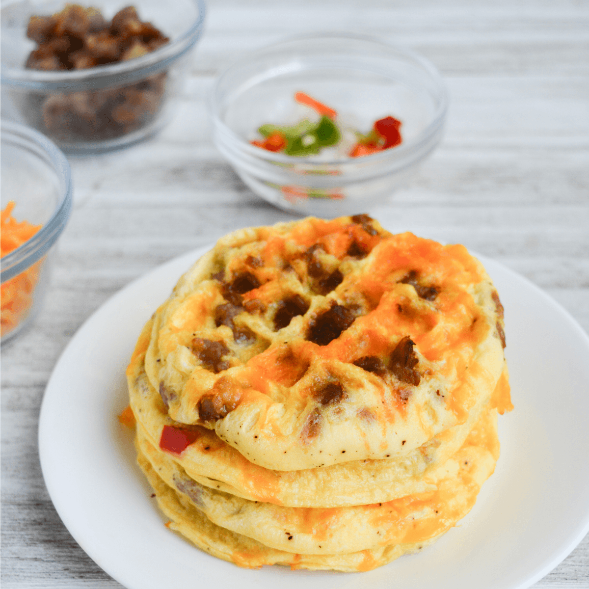 stack of waffle omelettes made using eggs, cheese, sausage, green bell peppers, red bell peppers and white onions