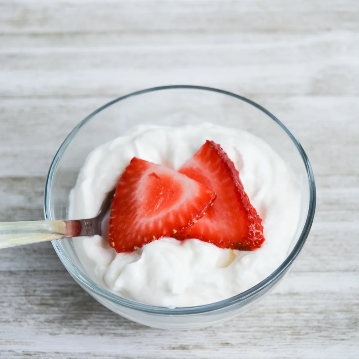 close up of serving of yogurt in a small bowl with a spoon, topped with sliced strawberries